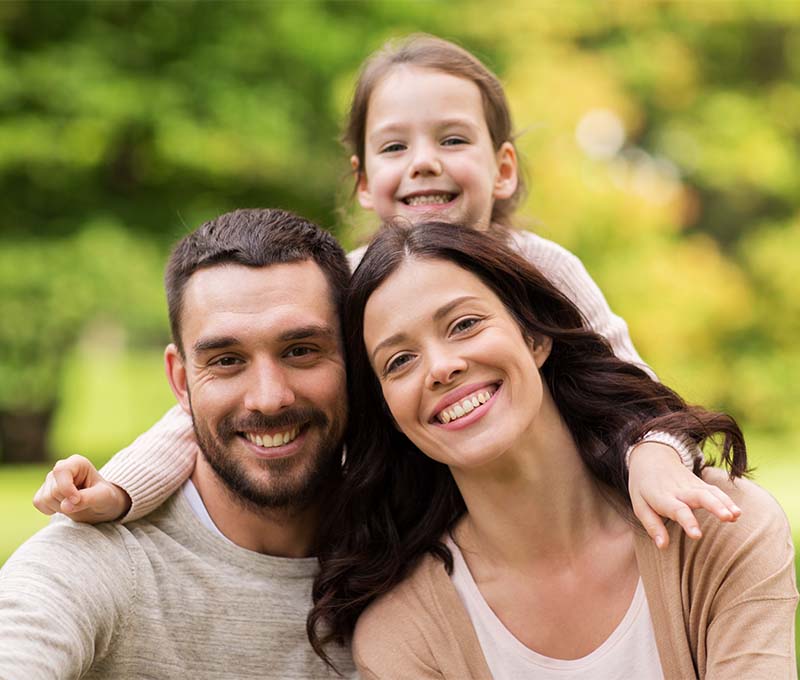 The image depicts a family of four posing outdoors with smiles on their faces.