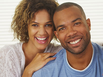 A man and woman posing together with smiles, the man wearing a blue t-shirt and the woman in a white top.